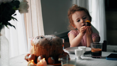 Little girl plays with homemade chocolate egg at the table decorated for Easterの写真素材