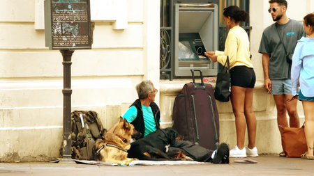 MARSEILLE, FRANCE - AUGUST 9, 2023. A beggar with dogs near ATM in the streetのeditorial素材