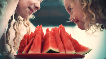 Small girls sniff ripe watermelon slices at homeの写真素材