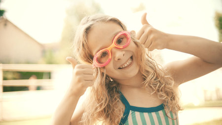 Smiling little blonde girl wearing swimming goggles shows thumbs up sign at outdoor swimming pool. Happy summer vacation timeの写真素材