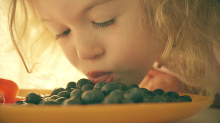Funny little girl tastes fresh blueberries on the plate, close-upの写真素材
