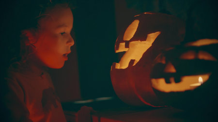 Curious girl looks at traditional Halloween pumpkins or jack olanterns in the darkの写真素材