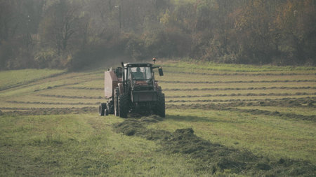Modern tractor with hay baler or hay maker collects cut grass in the field. Franceの写真素材