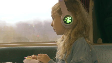 A little blonde girl listens to music through her headphones while traveling on a French trainの写真素材