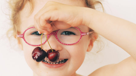 A Smiling Cheerful Girl with Glasses Enjoying Ripe Cherries on a Summer Dayの写真素材