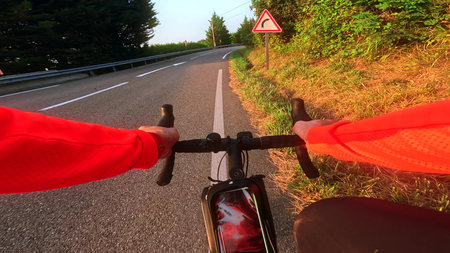 First person view of a cyclist riding along a mountain road at sunrise with a curve warning sign...