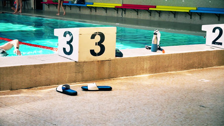 A French swimming pool with numbered starting blocks, sandals on the poolside. Calm training or...