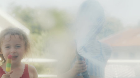 Children playing with water hose and eating ice cream on a hot summer dayの写真素材