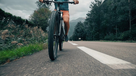 Electric bike rider in sportswear cycling on a mountain road. Low following camera angle from the front showing motion and scenic backgroundの写真素材