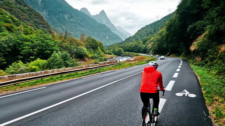 Cyclist riding along a scenic mountain road with lush forests and alpine peaks of Belledonne France....