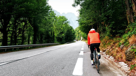 Cyclist riding on a mountain road in forest with following camera view, French Alpsの写真素材