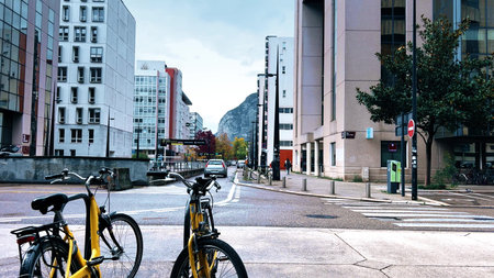 Modern street scene with bicycles and cars on Avenue Doyen Louis Weil in Grenoble, France, surrounded by contemporary architecture and autumn colors with mountains in backgroundの写真素材