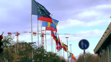 GRENOBLE, FRANCE - NOVEMBER 24, 2025. Row of national flags and EU flag along the street with construction cranes in backgroundのeditorial素材