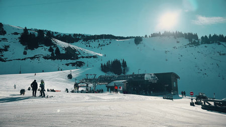 Sunny ski resort slopes, silhouettes of people and gondola station in Chamrousse, French Alps