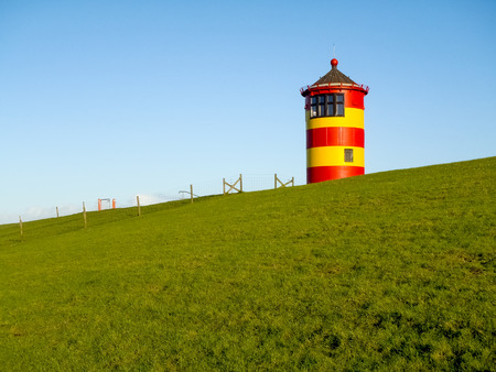 Pilsum, Germany - December 6, 2014: Lighthouse located near the coast especially for its colors in yellow and red stripes. It is located on a barrier of protection by the tides of the North Sea.の写真素材