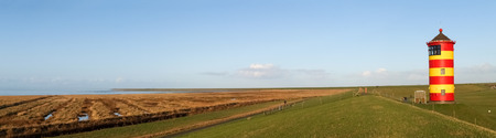 Pilsum, Germany - December 6, 2014: Lighthouse located near the coast especially for its colors in yellow and red stripes. It is located on a barrier of protection by the tides of the North Sea.の写真素材