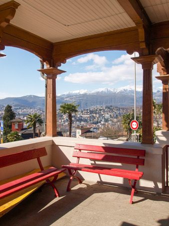 Lugano, Switzerland - March 01, 2015: Benches Waiting at the station of the funicular Lugano. The red benches are typical for the Swiss tradition. The old wooden station is open and overlooks the bay of the city.のeditorial素材
