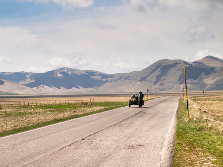 Italy, Castelluccio di Norcia - April 25, 2015: Motorcyclists on the road of big plan of Monti Sibillini. Motorcyclists in a vehicle sidecar salute as they pass.のeditorial素材