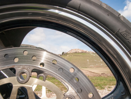Italy, Castelluccio di Norcia - april 24, 2015: Image of Castelluccio shot through the hoop front wheel of the motorcycle. The motorcycle is located on the roadside overlooking the floor dedicated to the cultivation of lentilsのeditorial素材