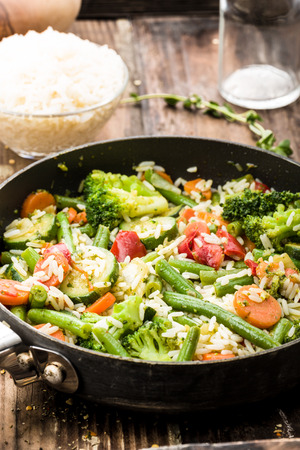 vegetable pan with fresh ingredients and rice on wooden undergroundの写真素材