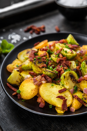 Fried potatoes with Brussels sprouts and bacon on a plateの写真素材