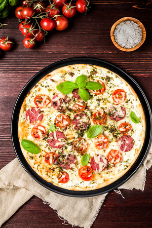 Pizza with cream cheese basil, tomato and salamiの写真素材