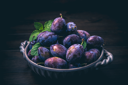 Plums in a bowl on wooden with mintの写真素材