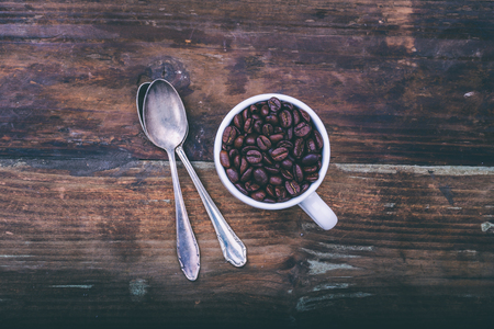 Coffee beans in a cup with spoon on wooden surfaceの写真素材