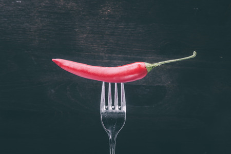 Hot pepper on a fork against a dark wooden backgroundの写真素材