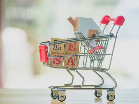Sale word written cube in shopping cart  home on wooden background. Concept for loan, property ladder, financial, mortgage, real estate investment, taxes and bonus.の写真素材