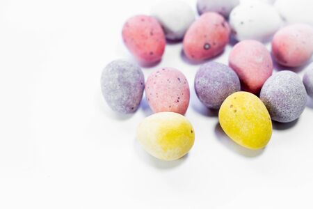 Sugar coated chocolate eggs, colorfull sweet easter treat. White background bright colours yellow,...