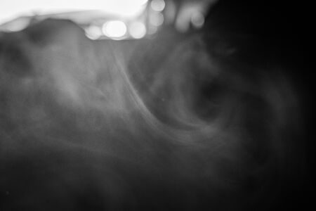 Smoke vapour smuges from e-cigarette in the sunlinght, black and white shot of smoking at home, vaping at home by the windowの写真素材