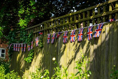 Union Jack bunting on a fence row, many flags in row on a string, front of garden VE day decorations in UK, memorial symbol of winning second world war, happy days in United Kingdomの写真素材