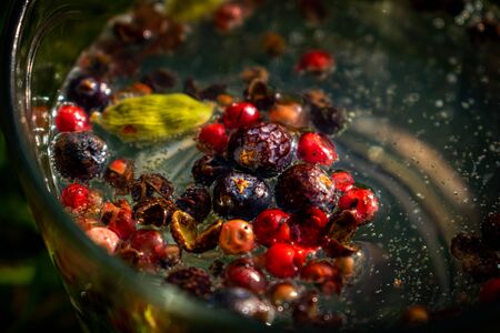Closeup on colorful various spice botanicals floating on top of the sparkling cocktail in the glass,...