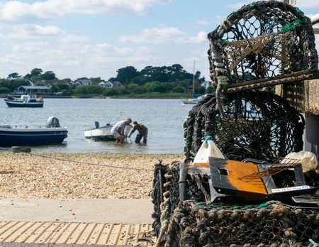 Mudeford Quay, United Kingdom - 16 July 2020: Two fishermen comming back from the sea fishing,...