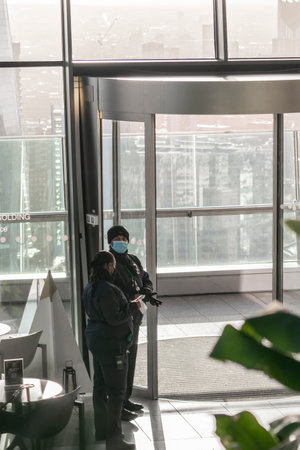 London, UK- 15 Dec 2020: Security guards in Sky Garden terrace at work wearing masks and gloves, man and woman standing in uniforms by the entrance to the view point.のeditorial素材