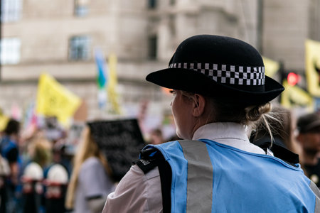 London,UK-28 Aug 2021: Blonde female police officer in London observing a large protest in the background.のeditorial素材