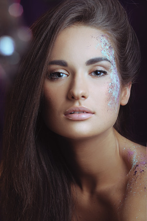Closeup portrait of beautiful girl with festive makeup in color spray and bokeh lightsの写真素材
