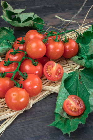 cherry tomatoes on a wooden surface with leaves of wood and hay.の写真素材