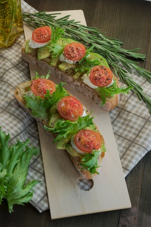 Avocado toast, cherry tomato on wooden background. Breakfast with toast avocado, vegetarian food, healthy diet concept.の写真素材
