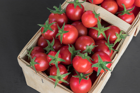 full top view of pile of cherry tomatoes in a rattan basket on black board for backgroundの写真素材