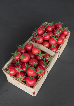 full top view of pile of cherry tomatoes in a rattan basket on black board for backgroundの写真素材