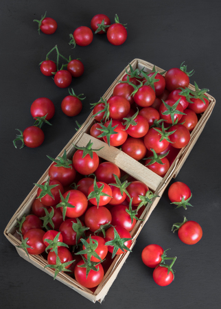 full top view of pile of cherry tomatoes in a rattan basket on black board for backgroundの写真素材
