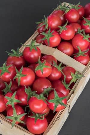 full top view of pile of cherry tomatoes in a rattan basket on black board for backgroundの写真素材