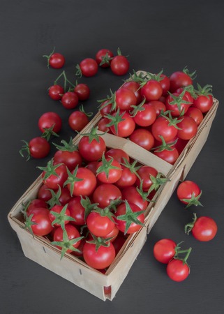 full top view of pile of cherry tomatoes in a rattan basket on black board for backgroundの写真素材