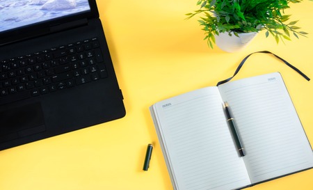 The minimum working space is a creative flat photo of the desktop. Top view office desk with laptop, notebook and datebook against yellow background. Top view with copy space, photos.の写真素材