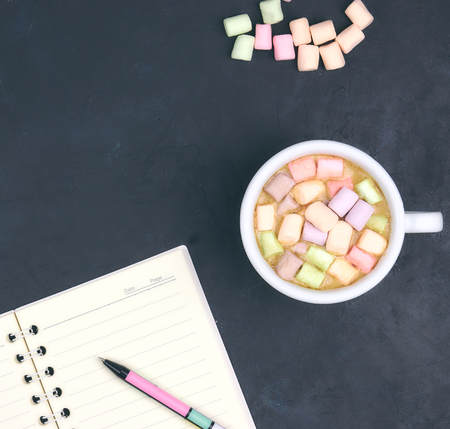 Cup with coffee and marshmallows, blank open notebook with pen on black concrete background. View from above. Flat layout. space for text. hot drink.の写真素材