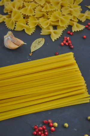 A variety of raw pasta next to the spices and spices on a black concrete background. View from above. close-up.の写真素材