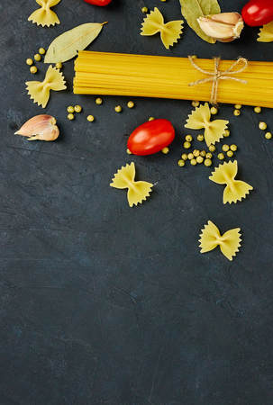 Frame for food. Pasta ingredients. Cherry tomatoes, spaghetti pasta, garlic and spices on a dark grunge background, copy space, top view. Italian pasta.の写真素材