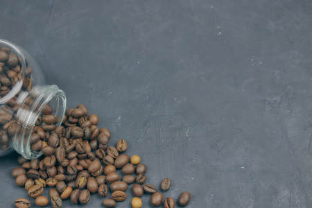 roasted coffee beans poured from a glass jar. angular placement of the coffee object. on dark concrete. horizontal view. copy spaceの写真素材